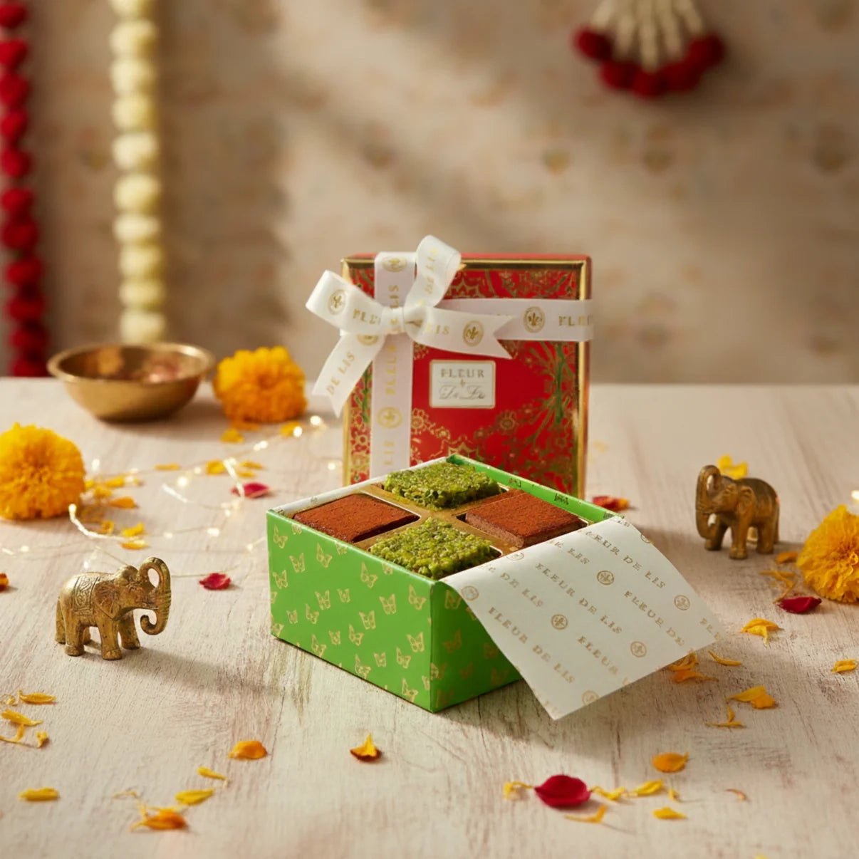 Open gift box with assorted cookies on a decorative table with flowers and small elephants.