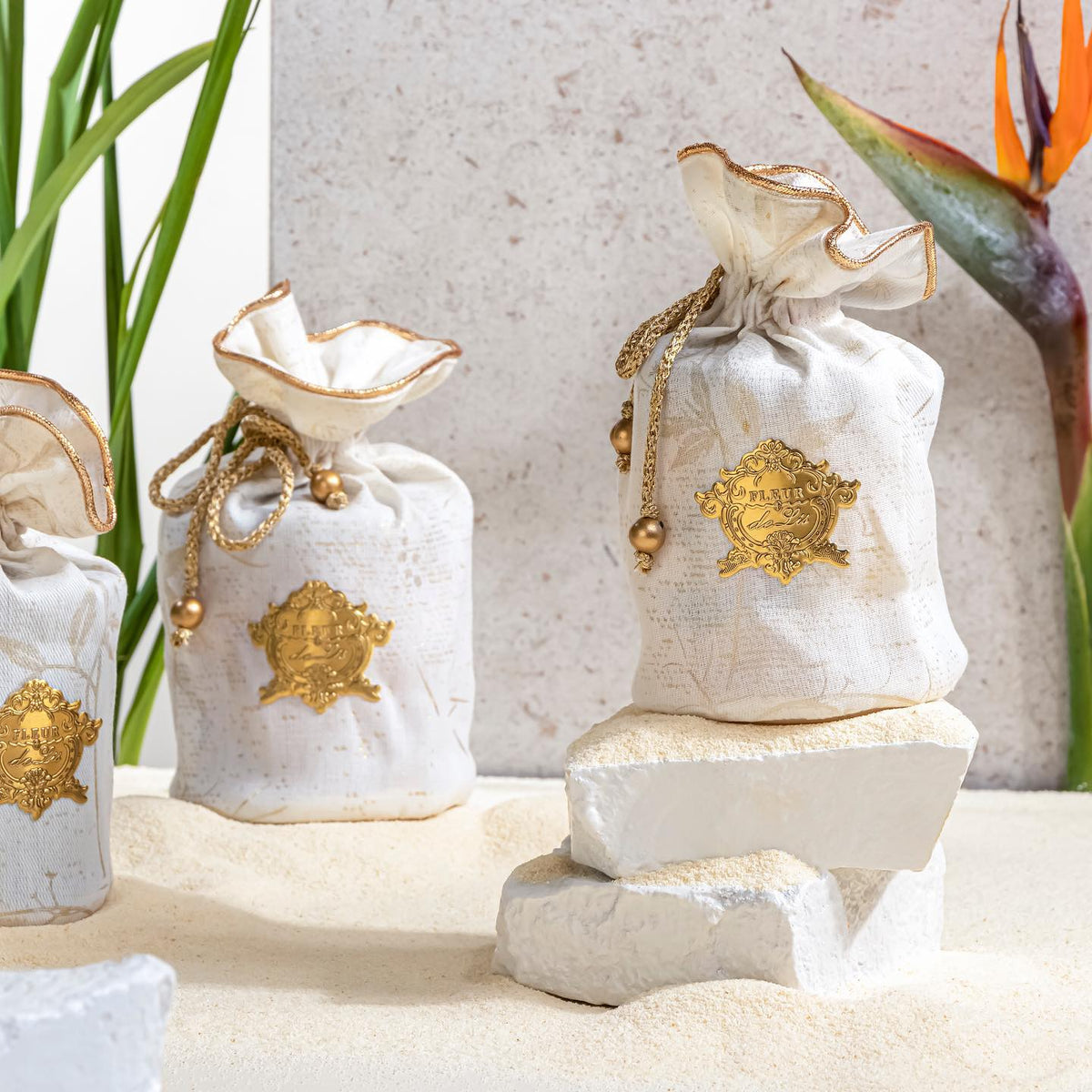 White bags with gold accents on a decorative stone surface with plants in the background