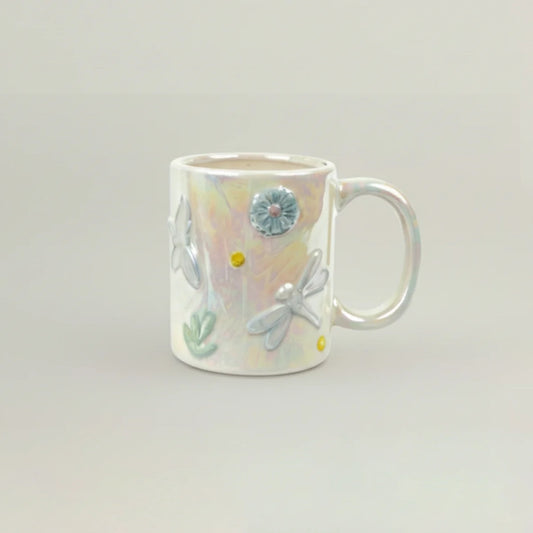 Ceramic mug with floral and dragonfly designs on a light gray background
