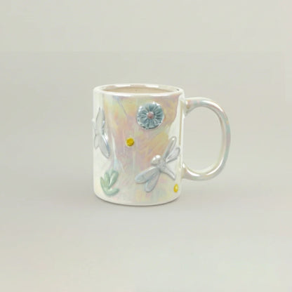 Ceramic mug with floral and dragonfly designs on a light gray background