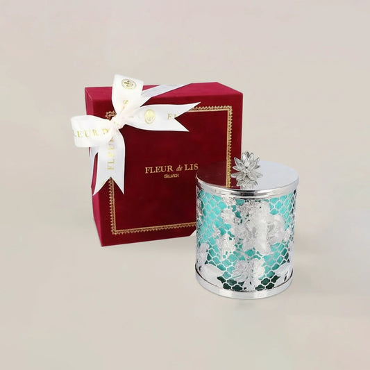 Decorative candle with silver floral design next to a red 'Fleur de Lis' box on a beige background