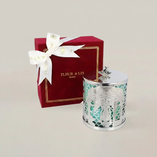 Decorative candle with intricate design next to a red 'Fleur de Lis' box on a light background