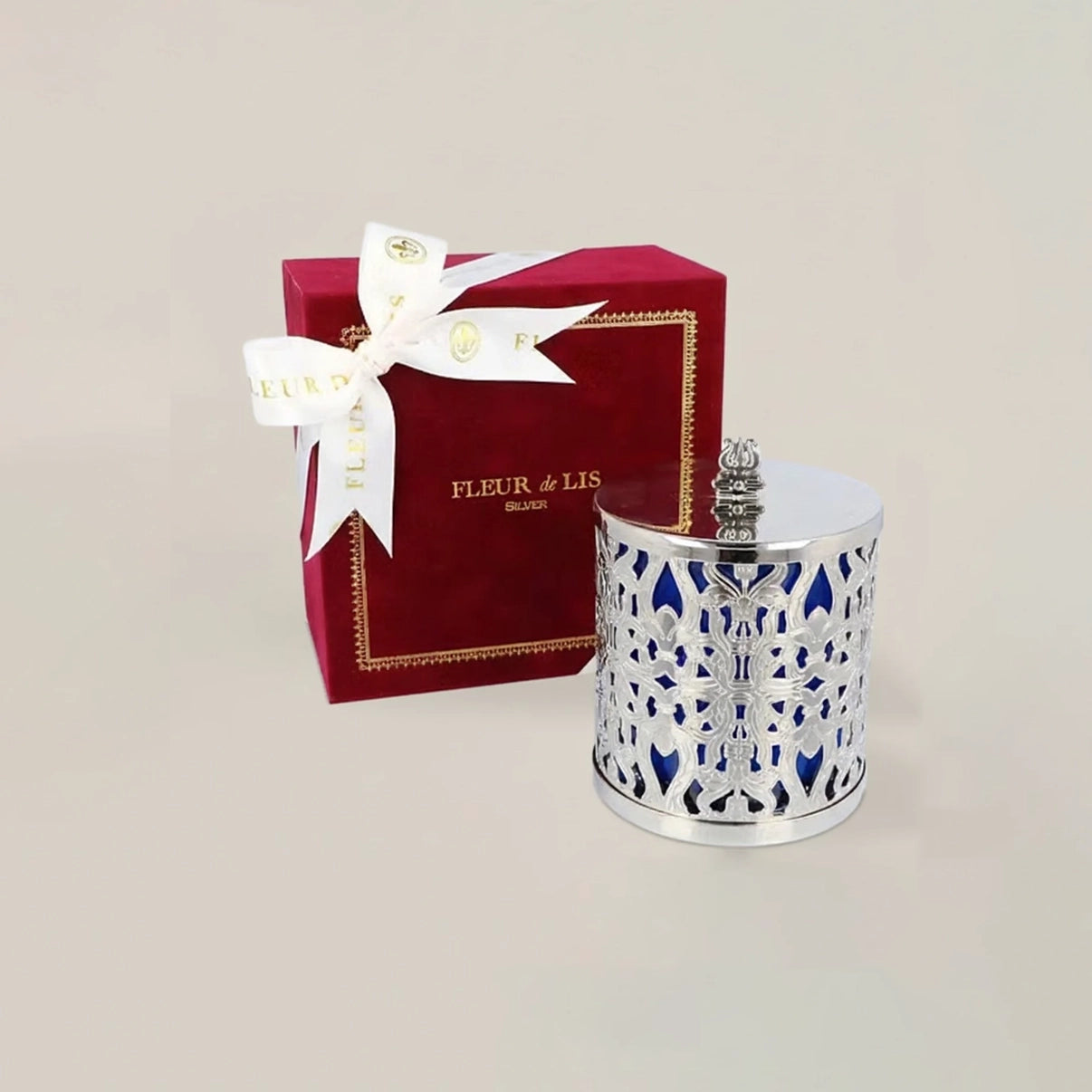 Silver candle holder with floral design next to a red 'Fleur de Lis' box on a light gray background