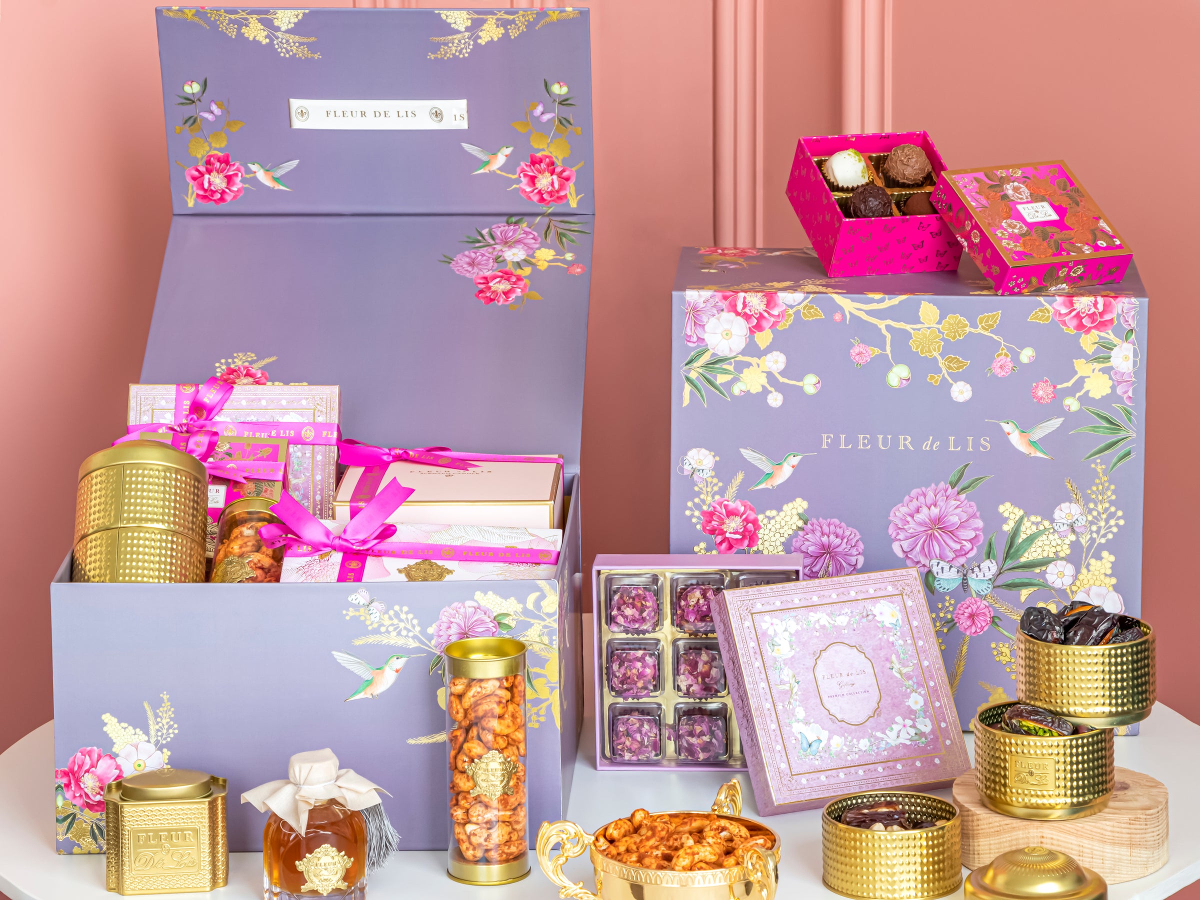 Gourmet gift set with floral boxes, chocolates, and tea on a pink background